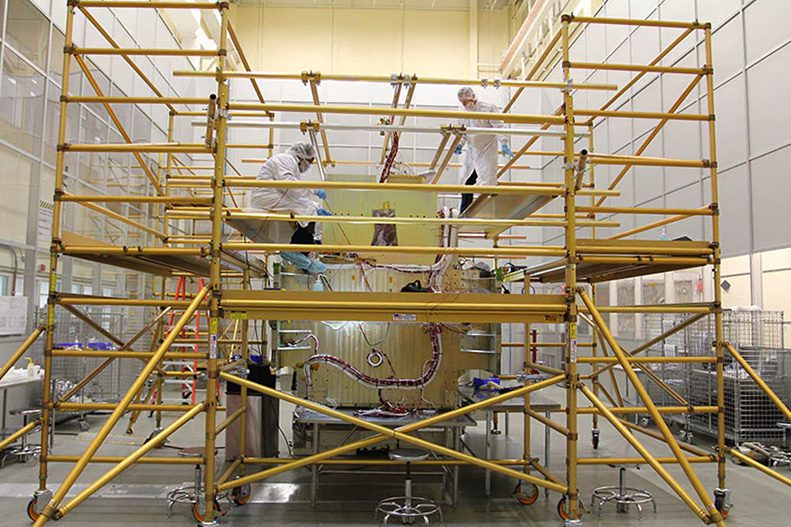 Workers on scaffolding painting a large mural indoors.