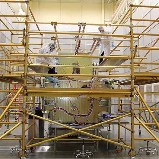 Workers on scaffolding painting a large mural indoors.